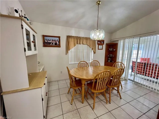 Dining space with light tile patterned flooring, vaulted ceiling, and an inviting chandelier