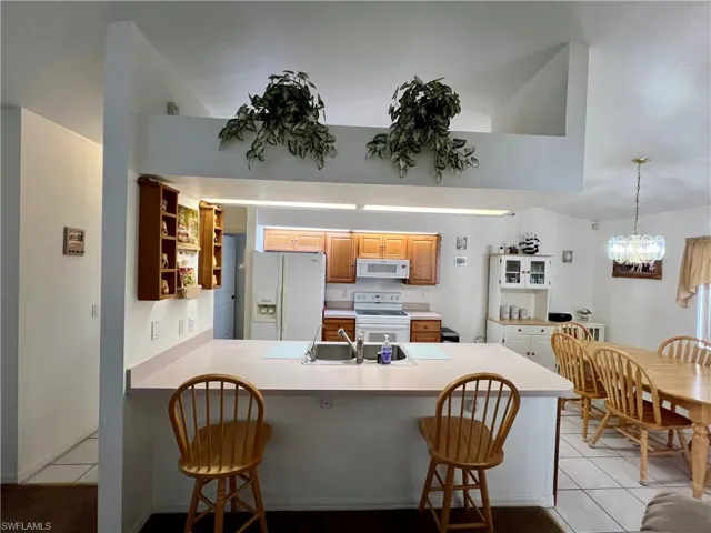 Kitchen featuring a breakfast bar, kitchen peninsula, light tile floors, appliances, and sink