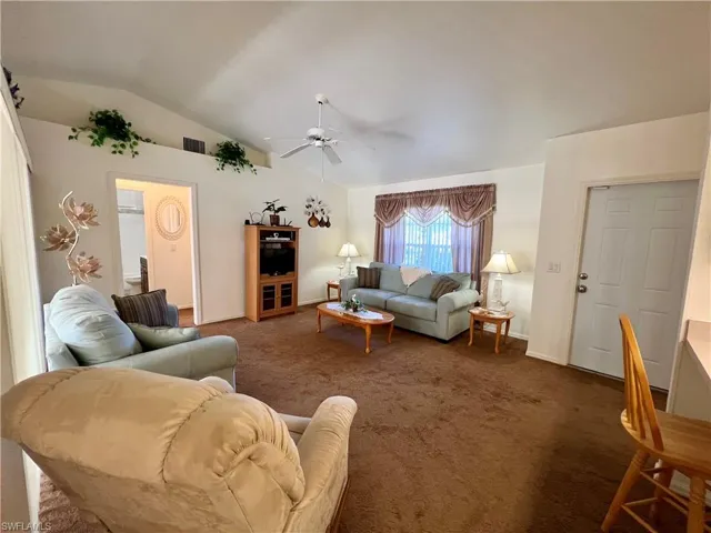 Carpeted living room with ceiling fan and vaulted ceiling