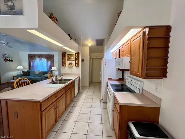 Kitchen featuring ceiling fan, sink, white appliances, and light tile patterned floors