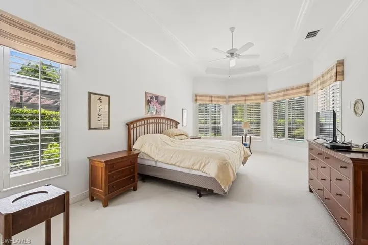 Bedroom featuring light colored carpet, crown molding, a tray ceiling, and a ceiling fan