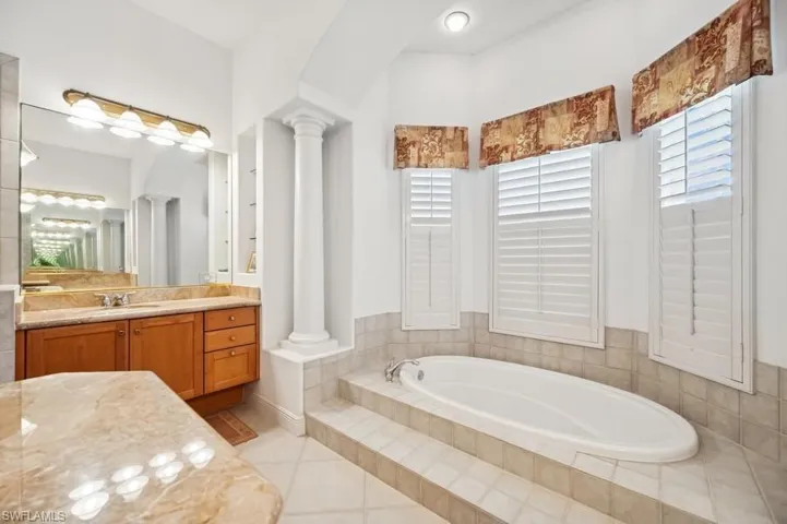 Bathroom with ornate columns, a garden tub, vanity, and tile patterned floors