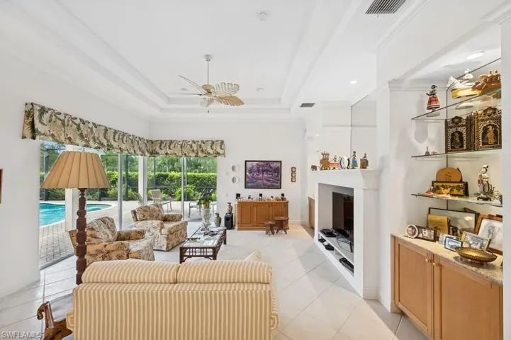 Living area featuring ceiling fan, light tile patterned floors, crown molding, a fireplace, and a raised ceiling