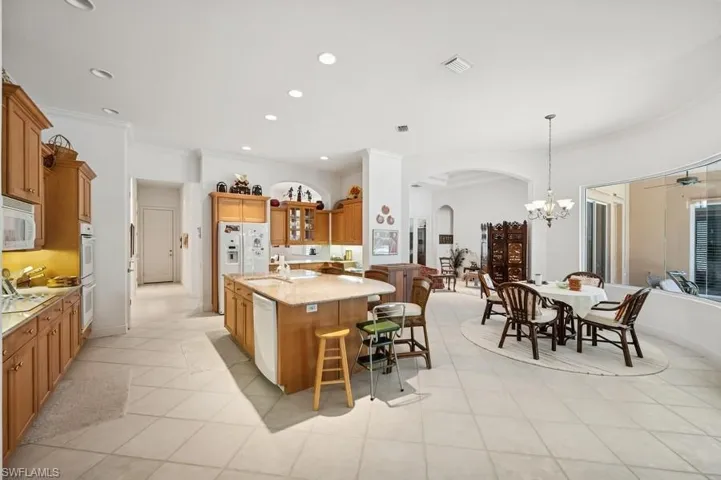 Kitchen with arched walkways, white appliances, a breakfast bar, brown cabinetry, and a center island with sink