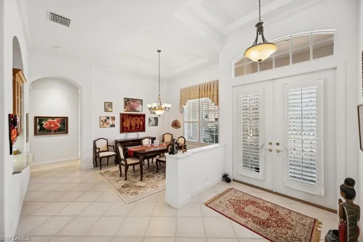 Foyer entrance featuring arched walkways, ornamental molding, light tile patterned floors, french doors, and a chandelier