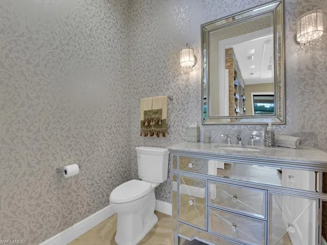 Bathroom featuring wallpapered walls, toilet, vanity, and baseboards