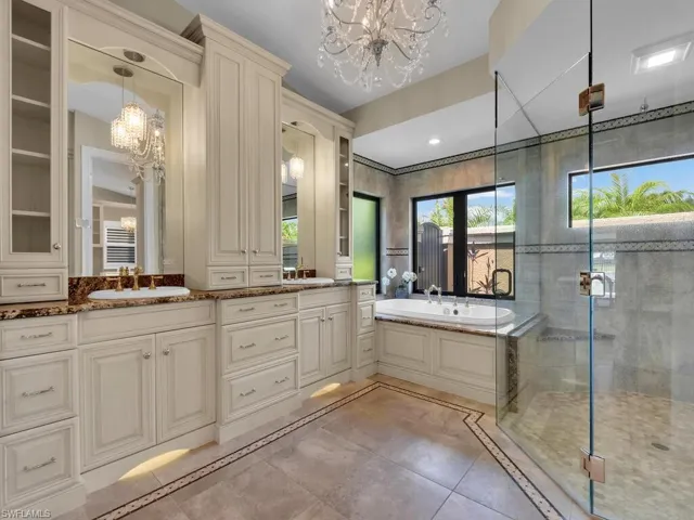 Full bath featuring a chandelier, inlaid floor details, double vanity, a shower stall, and a bath