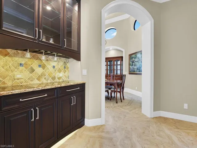 Bar with arched walkways, tasteful backsplash, baseboards, and light marble finish flooring