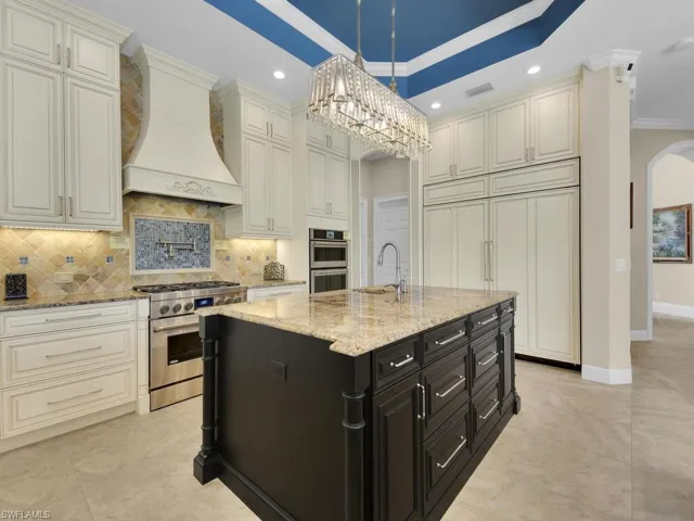 Kitchen with appliances with stainless steel finishes, custom range hood, a sink, ornamental molding, and backsplash