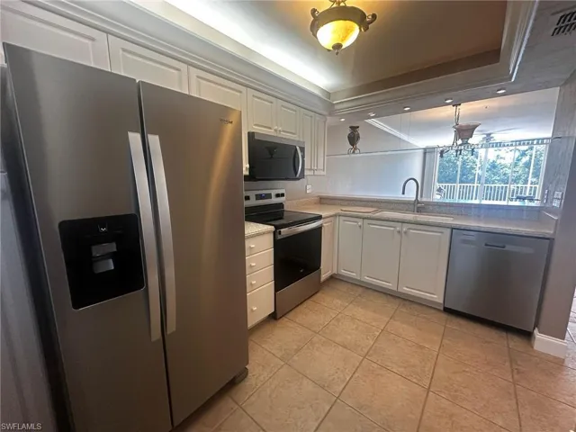 Kitchen featuring appliances with stainless steel finishes, white cabinets, a tray ceiling, light tile patterned floors, and hanging light fixtures