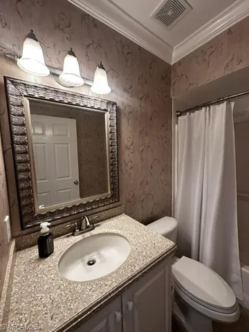Full bathroom with wallpapered walls, vanity, crown molding, and shower / bath combo