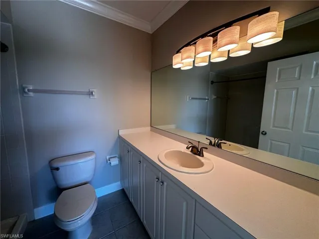 Bathroom with ornamental molding, vanity, tiled shower, and dark tile patterned floors