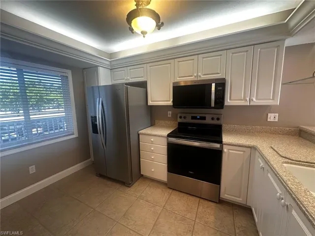 Kitchen featuring appliances with stainless steel finishes, light stone counters, and white cabinets