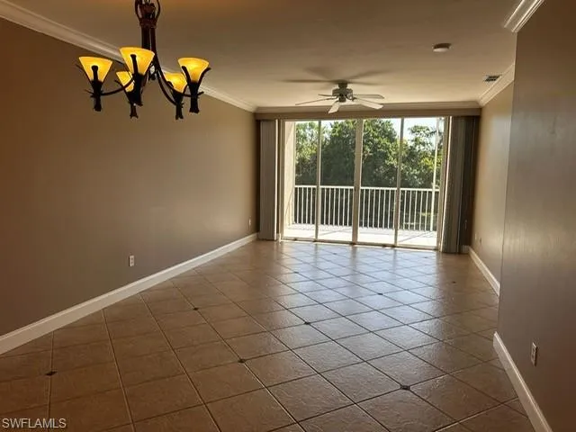 Empty room with crown molding, a chandelier, a wall of windows, light tile patterned flooring, and a ceiling fan