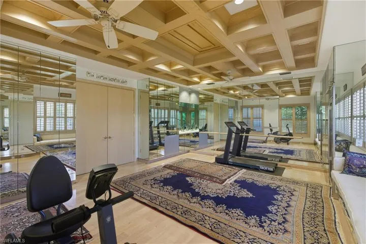 Workout area featuring coffered ceiling, ceiling fan, and beamed ceiling