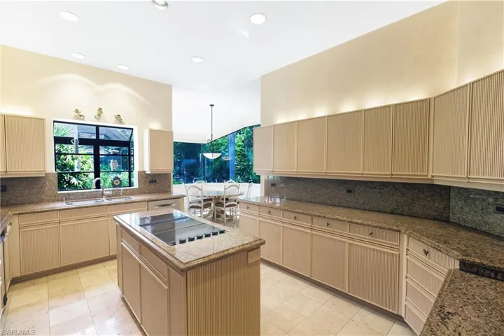 Kitchen with light brown cabinets, backsplash, an island with sink, and recessed lighting