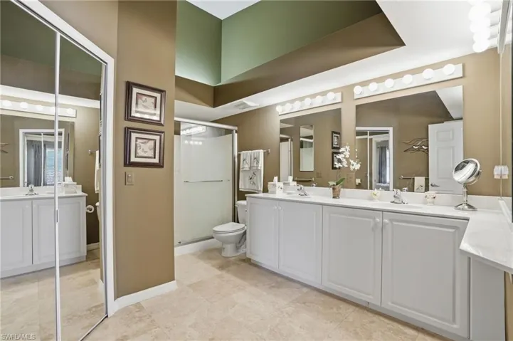 Bright en-suite bath featuring dual sinks, a walk-in shower, and plenty of storage.