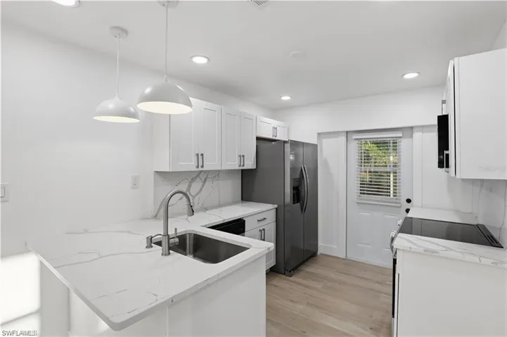 Kitchen featuring white cabinetry, stainless steel appliances, light stone counters, light wood finished floors, and a peninsula