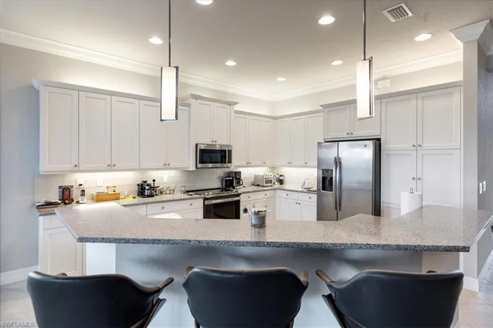 Kitchen featuring stainless steel appliances, decorative backsplash, a kitchen breakfast bar, and decorative light fixtures