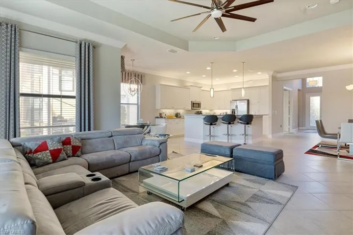 Tiled living room with crown molding and ceiling fan with notable chandelier