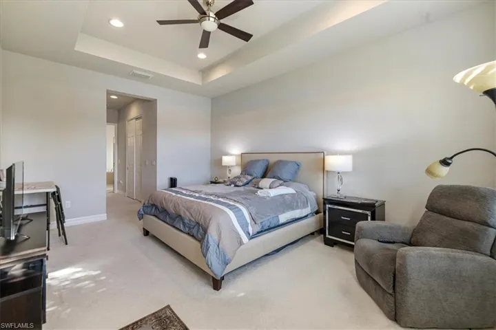 Bedroom featuring ceiling fan, a raised ceiling, and light colored carpet