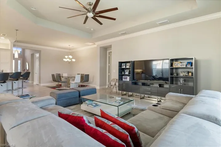 Living room with ornamental molding, ceiling fan with notable chandelier, and a tray ceiling
