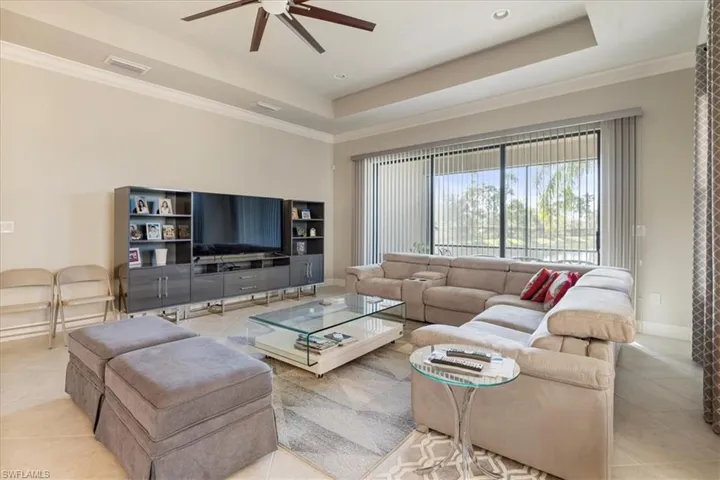 Living room featuring a raised ceiling, light tile patterned flooring, and crown molding