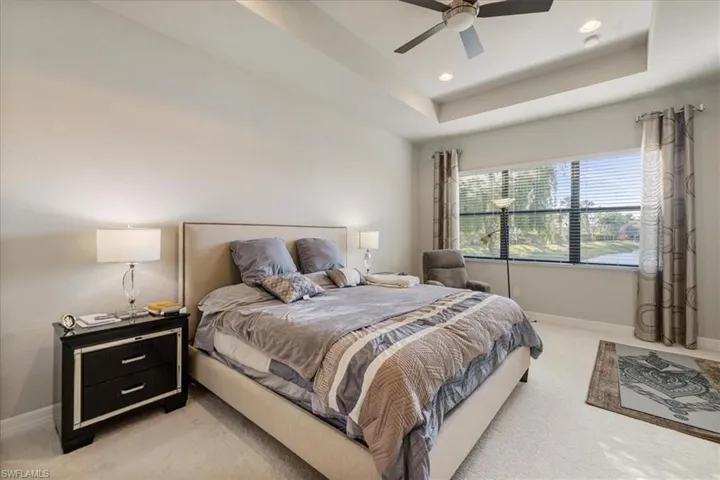 Carpeted bedroom with ceiling fan and a tray ceiling