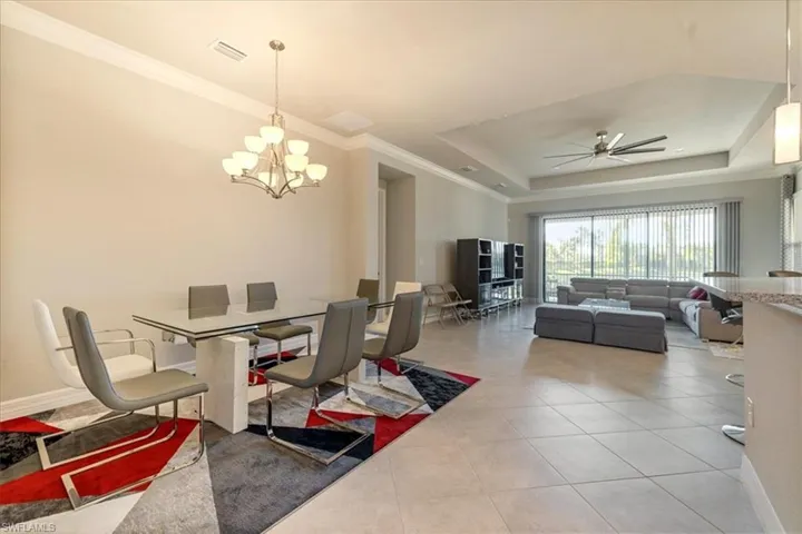 Dining space featuring crown molding, tile patterned floors, a tray ceiling, and ceiling fan with notable chandelier