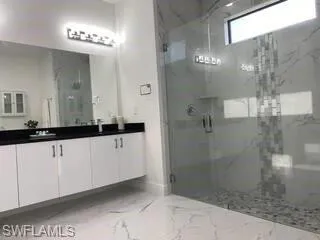 Full bath featuring marble tiled flooring, double vanity, and a marble finish shower
