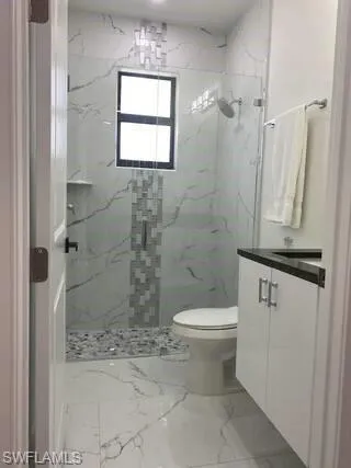 Full bath featuring marble look tiles, vanity, and a marble finish shower