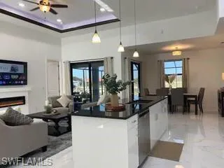 Kitchen with light marble finish floors, ceiling fan, dark countertops, a tray ceiling, and open floor plan