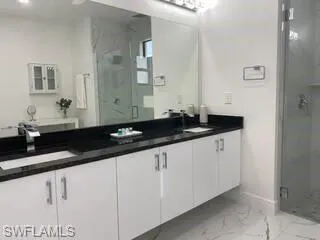 Bathroom with a shower stall, double vanity, and marble look tiles