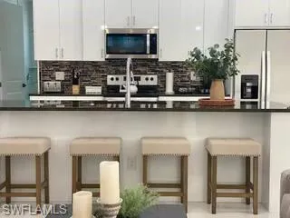 Kitchen with dark countertops, appliances with stainless steel finishes, a kitchen breakfast bar, white cabinetry, and backsplash
