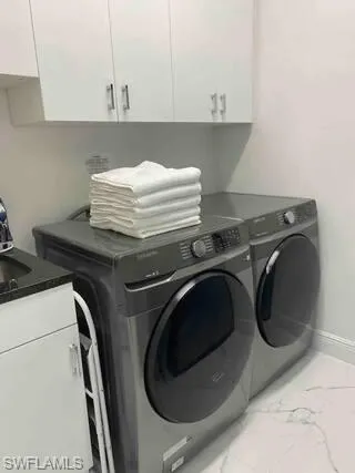 Laundry room with cabinet space, washing machine and dryer, and light marble finish floors
