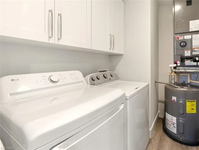 Laundry room featuring electric water heater, light wood-type flooring, heating unit, washer and dryer, and cabinet space