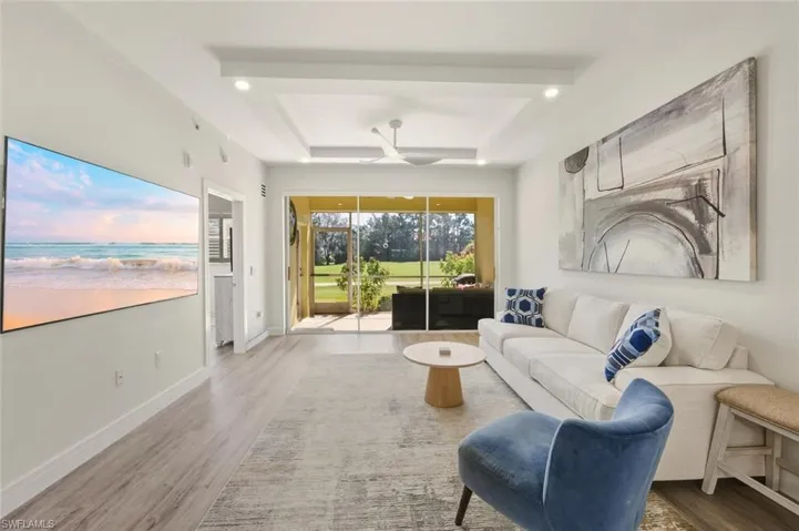 Living area with vinyl plank flooring, a tray ceiling, ceiling fan, and recessed lighting