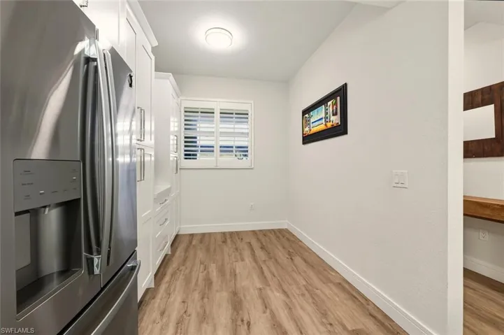 Kitchen featuring stainless steel refrigerator with ice dispenser, white cabinets, light wood-type flooring, and light countertops