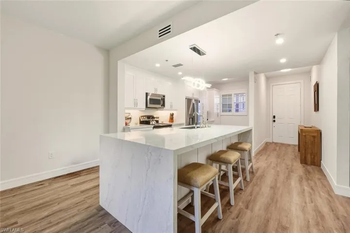 Kitchen featuring a breakfast bar area with quartz waterfall counter tops, pendant lighting, white cabinetry, stainless steel appliances, and extra storage under bar