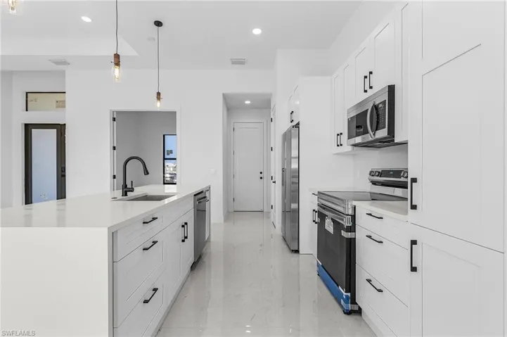 Kitchen featuring an island with sink, appliances with stainless steel finishes, marble finish floor, white cabinetry, and a sink