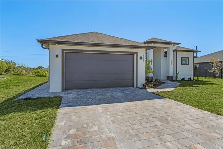 Prairie-style house with stucco siding, decorative driveway, a front yard, and fence