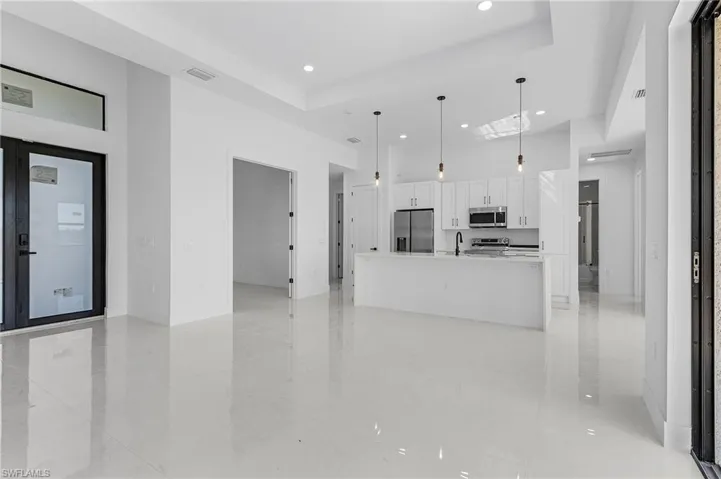 Kitchen with visible vents, decorative light fixtures, a large island with sink, appliances with stainless steel finishes, and white cabinets