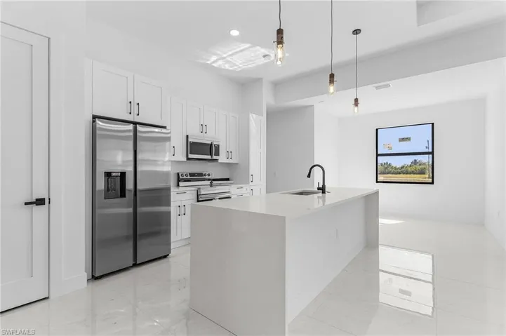 Kitchen with decorative light fixtures, light countertops, stainless steel appliances, white cabinetry, and a sink
