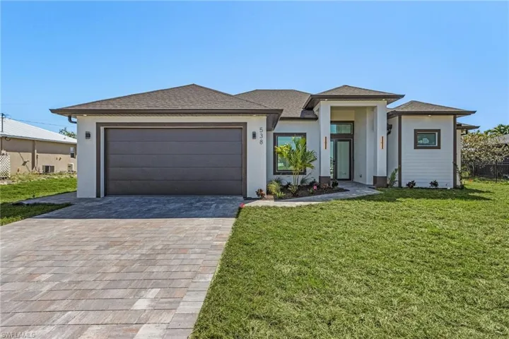 Prairie-style house with a front yard, roof with shingles, stucco siding, decorative driveway, and an attached garage