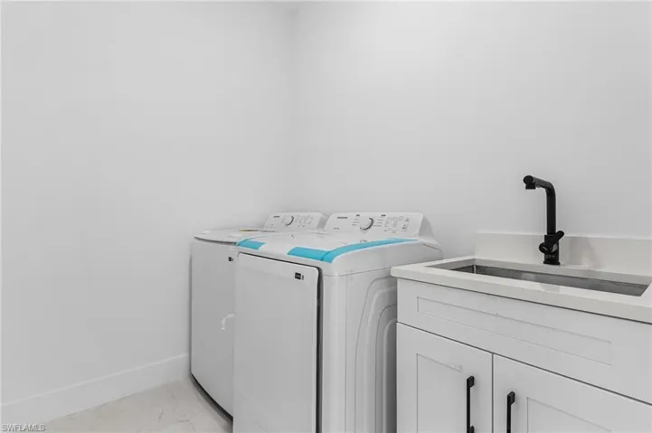 Laundry room featuring marble finish floor, a sink, washing machine and dryer, cabinet space, and baseboards