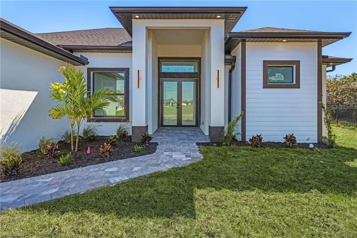 Property entrance with fence, a yard, a shingled roof, stucco siding, and french doors