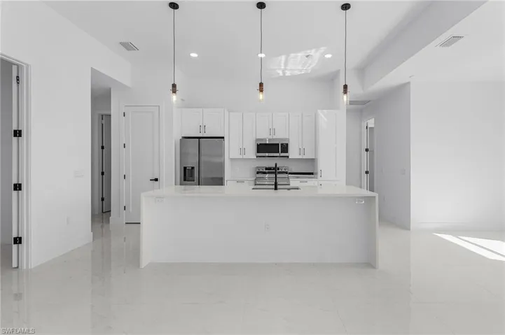 Kitchen featuring visible vents, an island with sink, white cabinets, stainless steel appliances, and a sink