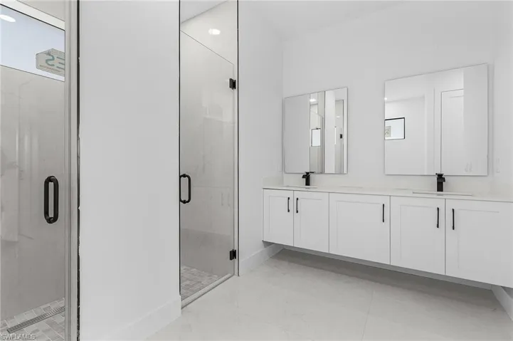 Full bathroom with a sink, baseboards, double vanity, and a shower stall