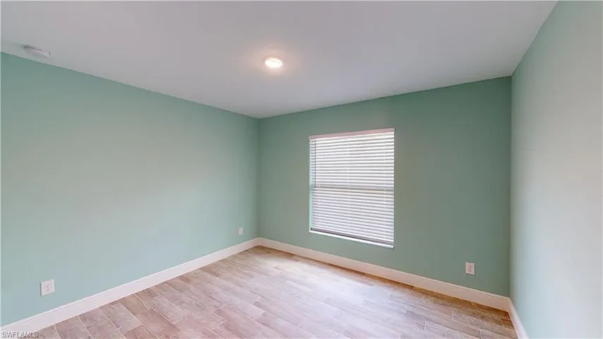 Empty room with light wood-style flooring and a smoke detector