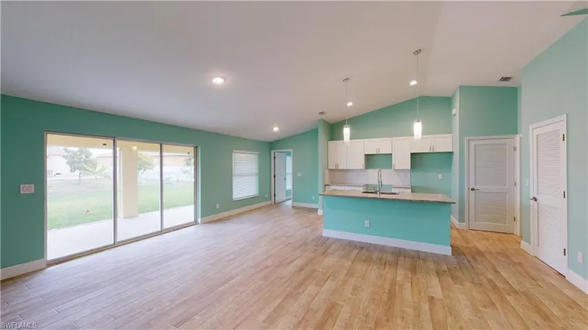 Kitchen featuring a kitchen island with sink, lofted ceiling, hanging light fixtures, light wood finished floors, and white cabinets
